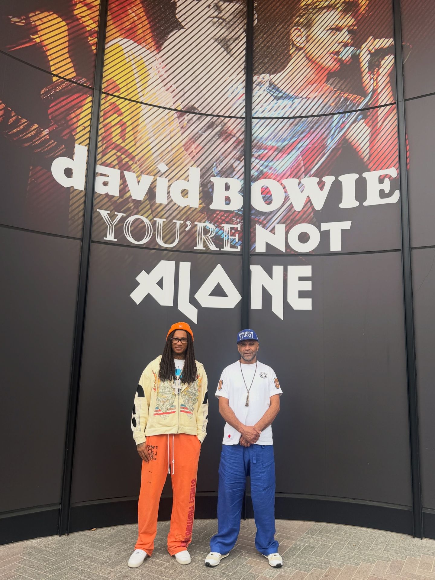 Digga and another person beneath the David Bowie You’re Not Alone display