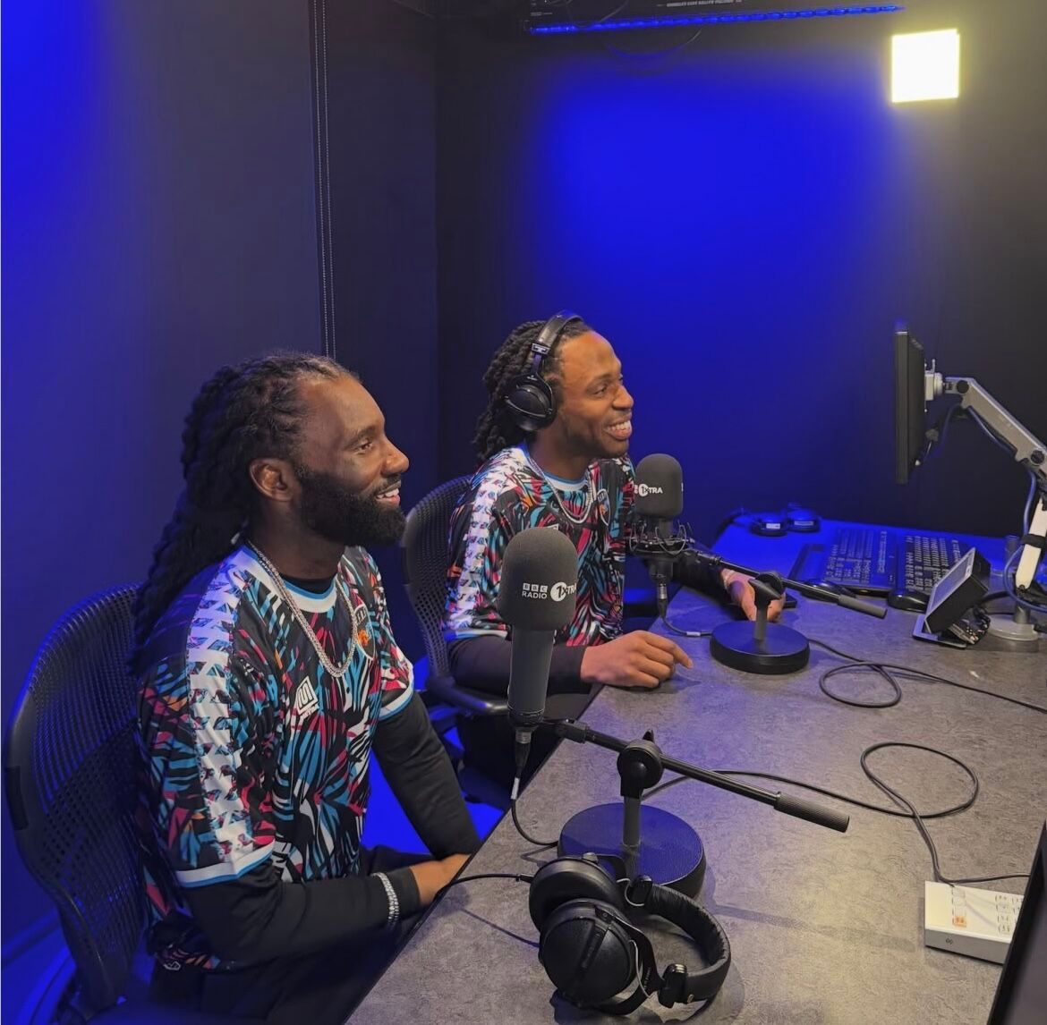 Wretch 32 and Avelino sitting at microphones during a radio interview